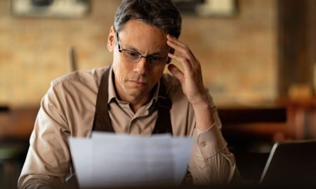 distraught small business owner reading reports while going through paperwork bar