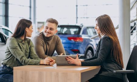 young couple talking sales person car showroom