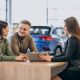young couple talking sales person car showroom