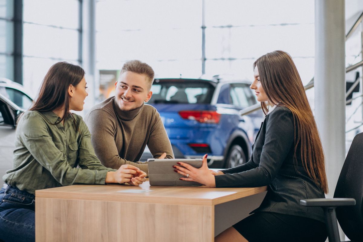 young couple talking sales person car showroom