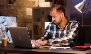 businessman typing laptop searching through documents while working from home office